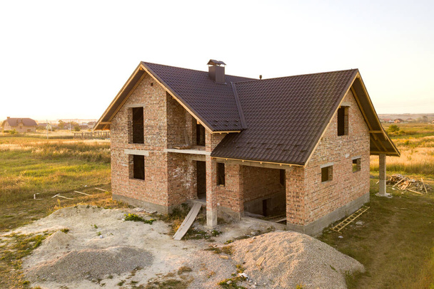Casa de tijolo inacabada com estrutura de telhado de madeira coberta com folhas de telha de metal em construção
. - Foto, Imagem