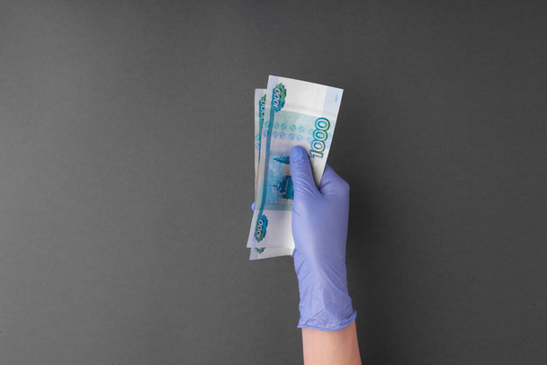 Female hand in latex rubber glove holds out money, banknotes russian rubles - Foto, Imagen