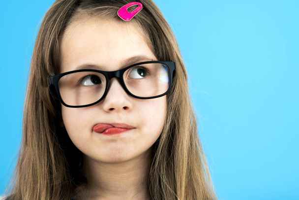 Close up portrait of a funny child school girl wearing looking glasses isolated on blue background. - Photo, Image