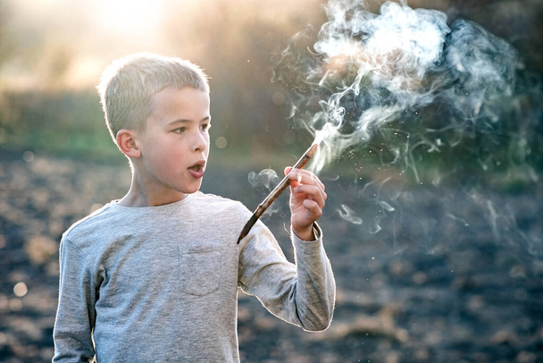 Child boy playing with smoking wooden stick outdoors. - Fotó, kép