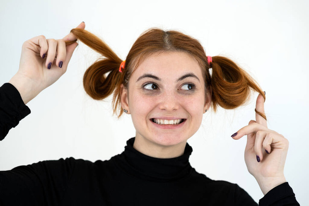Retrato de cerca de una divertida adolescente pelirroja con peinado infantil sonriendo felizmente aislada en el fondo blanco
. - Foto, Imagen
