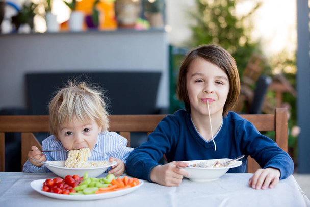Cute children, boy brothers, eating spaghetti in garden summertime - Φωτογραφία, εικόνα