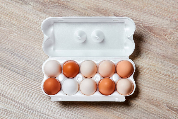 huevos de diferentes tonos de blanco a marrón se embalan juntos en una caja de huevo en una superficie de mesa de madera, vista superior horizontal
 - Foto, imagen