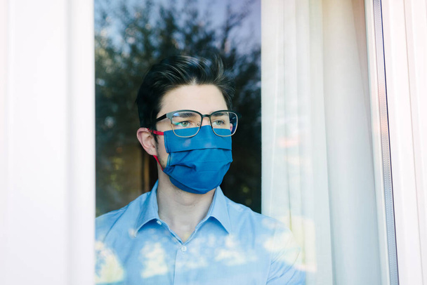 Young businessman with mask forced to stay in quarantine at home for Corona virus looking out window. - Fotoğraf, Görsel