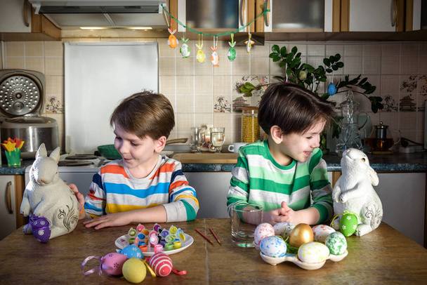 Dos niños pequeños para colorear huevos para las vacaciones de Pascua en la cocina doméstica, en el interior. Hermanos hermanos divirtiéndose y celebrando fiesta. - Foto, imagen