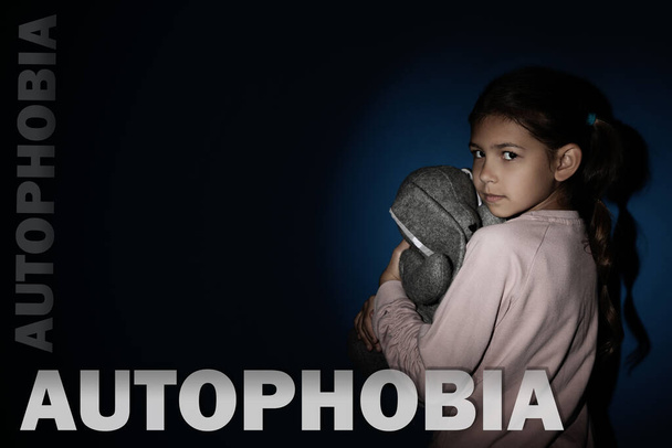 Sad little girl with toy near blue wall. Autophobia - Фото, зображення