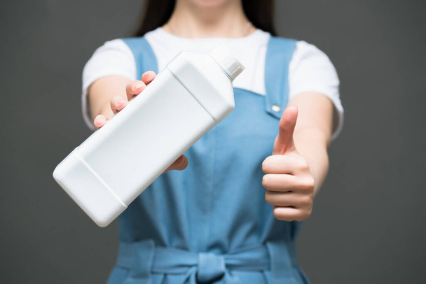 Woman with detergent bottle on gray background close up. - Φωτογραφία, εικόνα