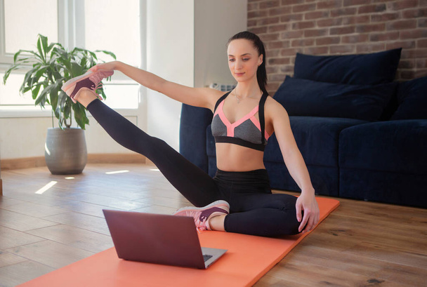 Woman training at home, doing exercises and watching videos on laptop, training in living room. Body care concept.  - Photo, image