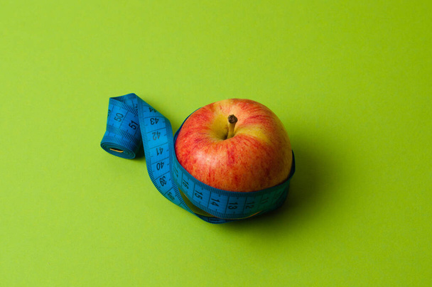 An apple on green background and a centimeter. Healthy eating, calorie count and weight loss concept - Photo, image