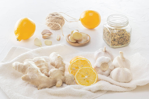 Ingwer, Knoblauch, Zitrone und eine trockene medizinische Kamille im Glas - ein Mittel zum Schutz vor Virusinfektionen und Erkältungen auf einem hellen Holztisch. - Foto, Bild
