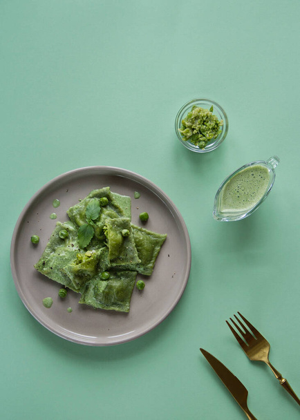 Green ravioli on a plate on a green background with sauce and appliances, top view. - Foto, imagen