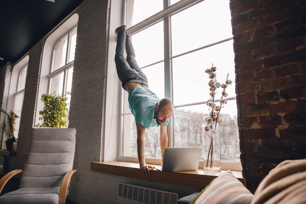 Young man doing yoga at home while being quarantine and freelance working - 写真・画像