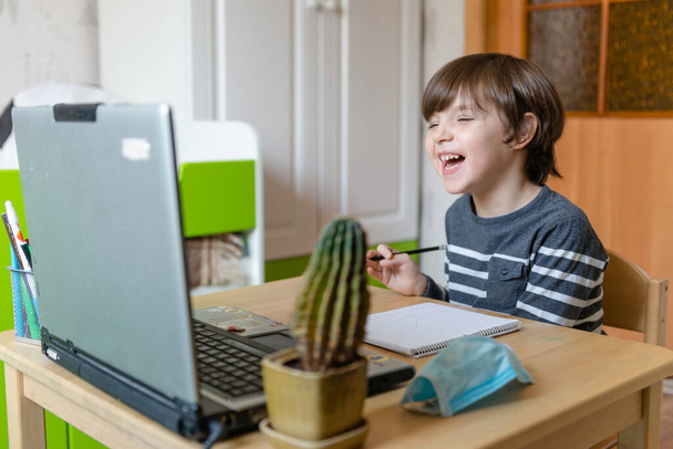 Etäopetus lapsille sepelvaltimotautiepidemian aikana. Poika istuu pöydässä ja suorittaa opettajan tehtäviä Internetissä.. - Valokuva, kuva