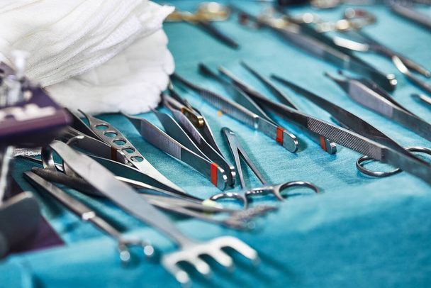 Instrumentos quirúrgicos en el quirófano, dispuestos sobre una mesa estéril sobre un tejido azul especial. El concepto de medicina, cirugía, área estéril. Cirugía plástica. Enfoque selectivo
. - Foto, imagen