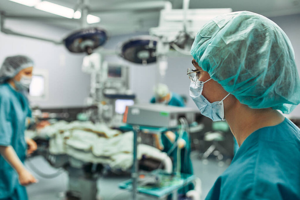 Портрет женщины-хирурга, операция на заднем плане. Концепция хирургической медицины. Женщина-хирург, равенство полов, спасение жизней. красота и здоровье
 - Фото, изображение