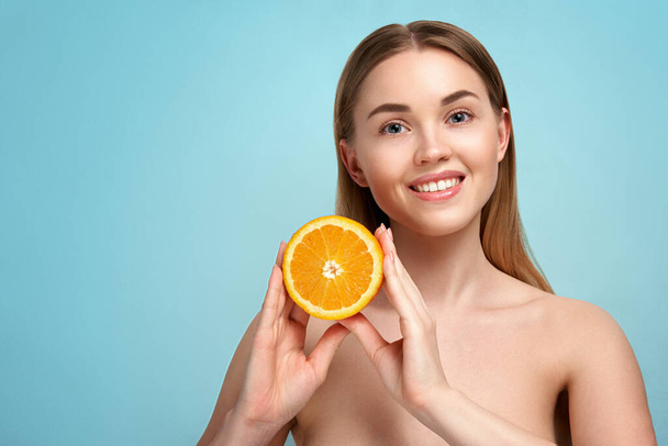 Pretty charming joyful attractive cheerful funny comic positive nude natural pure girl having two pieces of orange, on blue background. isolated on beige background with copy space for advertisement. Skincare. Vitamin C. Blonde woman - Zdjęcie, obraz