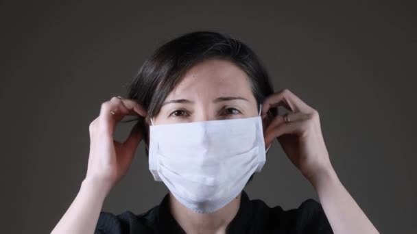 Beyaz bir tıbbi maske takan ve çıkartan beyaz bir kadının portresi. Bulaşıcı hastalıklara karşı koruma, koronavirüs. - Video, Çekim