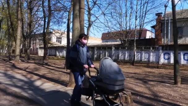 Ein maskierter Mann läuft mit einem Kinderwagen durch einen Park. Coronavirus. Kyev. Ukraine - Filmmaterial, Video