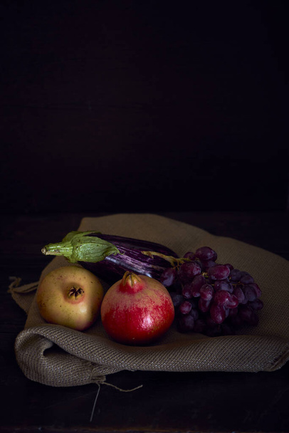 вертикальний натюрморт з баклажанами та гранатами з виноградом на мокрій тканині темне освітлення
 - Фото, зображення