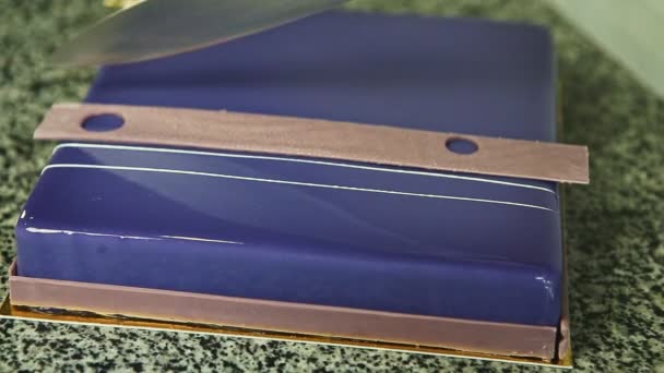 Руки крупным планом разрезают пополам ножом весь фиолетовый глазированный квадратный торт из мусса
 - Кадры, видео