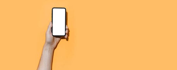 Ανδρικό hand holding smartphone με mockup σε πανοραμικό φόντο παστέλ πορτοκαλί χρώμα με χώρο αντιγραφής. - Φωτογραφία, εικόνα
