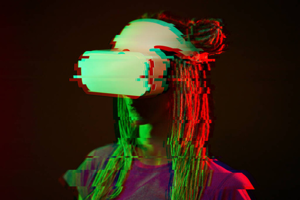 Woman is using virtual reality headset. Neon light studio portrait. Image with glitch effect. - Foto, afbeelding