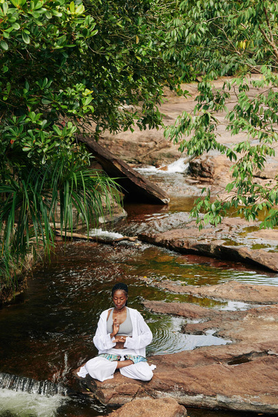Ruhige Schwarze meditiert am plätschernden Bach und hält ihre Hände in Suren und Gyan-Mudras - Foto, Bild