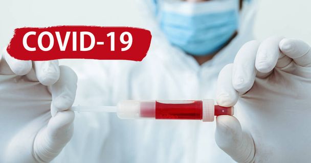 Text covid-19 on red warning sign. Coronavirus blood test in doctors hands. Doctor in protective medical suit, biological hazard, mask on white background. Concept of medicine laboratory health care. - Foto, Imagen