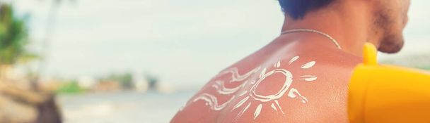 Mężczyzna na plaży z filtrem przeciwsłonecznym na plecach. Skupienie selektywne. - Zdjęcie, obraz