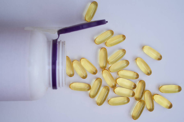 Gelbe Pillen aus einem Glas auf weißem Hintergrund verschüttet - Foto, Bild