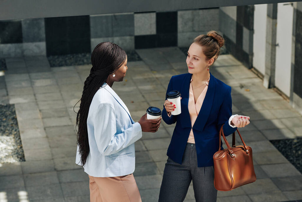 Ofis binasının önünde dikilen iki genç iş kadını kahve içip, haberleri ve dedikoduları tartışıyor. - Fotoğraf, Görsel