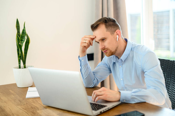 Guy in a formal shirt with airpods uses a laptop - Fotoğraf, Görsel
