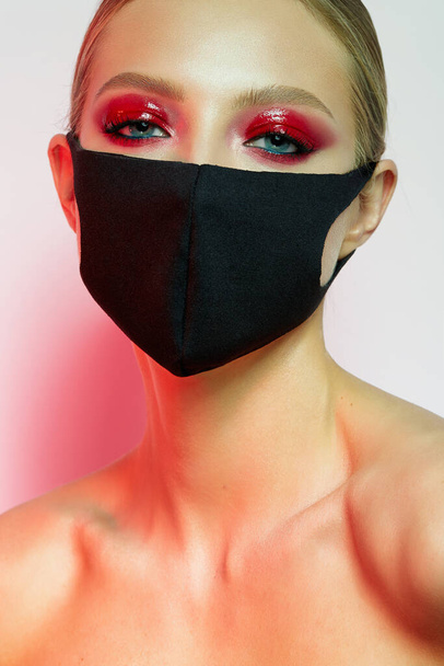 Beautiful girl with bright creative make-up. Young model in a black mask on her face. Coronavirus protection. Beauty face. Photo taken in the studio. - Fotografie, Obrázek