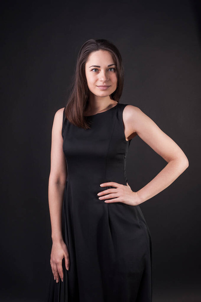 Elegant nice girl is posing with hand on her waist. Elegant black dress, so dark everywhere. Amazing girl with attractive appearance - Foto, imagen