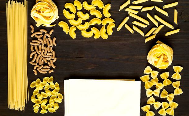 Diverse ongekookte pasta op houten ondergrond. Voedselconcept. Plat gelegd. Close-up, kopieerruimte. - Foto, afbeelding