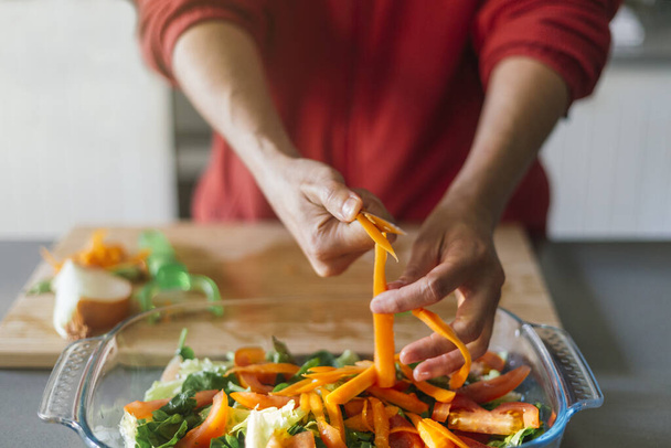 Frau schneidet Möhren und legt sie mit den Händen in einen Salat - Foto, Bild