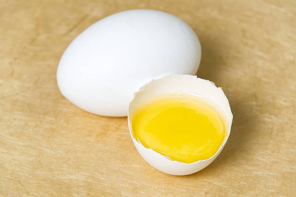 jaja kurze białe z połową rozbitego jaja na beżowym teksturowanym tle - Zdjęcie, obraz