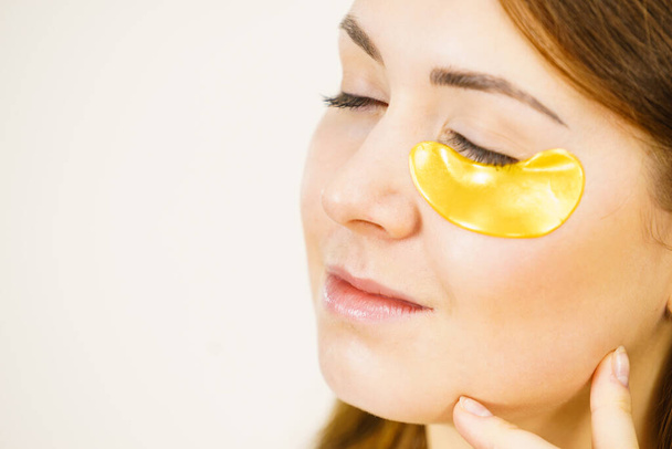 Young woman applying golden collagen patches under eyes. Mask removing wrinkles and dark circles. Girl taking care of delicate skin around eye. Beauty treatment. - Foto, imagen
