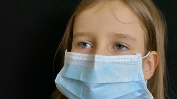 Éclosion de Coronavirus Covid-19. Petite fille blonde portant un masque jetable bleu clair pour la protection du virus sur fond noir en studio. Concept de quarantaine
 - Séquence, vidéo