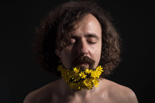 Stúdió drámai portré egy harminc éves fiatalemberről, csukott szemmel. a sárga virágokat göndör hajba és hosszú szakállba szőtték. Fogalma tavaszi virágok szakállas. Virágok és tavasz. Barna hajú, göndör hajú fiatalember. Brutális bea - Fotó, kép