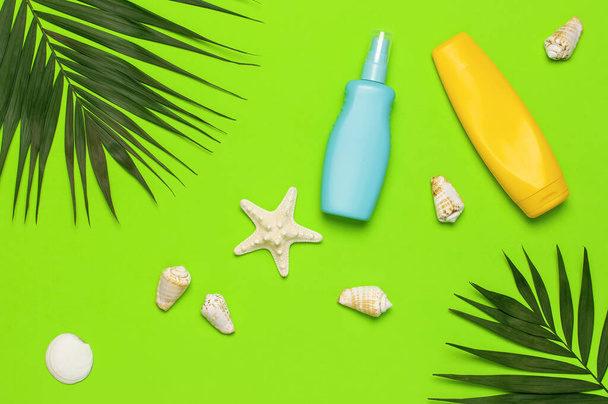 Sun protection Summer background vacation travel concept Yellow blue bottles of sunscreen cream tropical palm leaves shells starfish on green background top view flat lay copy space. Summer cosmetics. - Fotografie, Obrázek