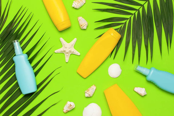 Ochrona przed słońcem Summer background holiday travel concept Yellow blue bottles of sunscreen cream tropical palm leaves shells starfish on green background top view flat lay copy space. Kosmetyki letnie. - Zdjęcie, obraz