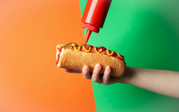 Person pouring ketchup on hot dog, on two tone background - Photo, Image