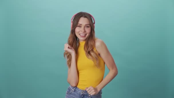 Happy young girl dancing in headphones isolated on a blue background - Video