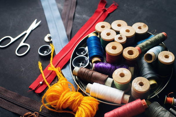 Sewing kit accessories for handicraft or needlework on dark stone table, colorful threads, home hobby and quarantine concept,  selective focus - Photo, image