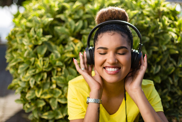 Красивая молодая чернокожая американка слушает музыку в наушниках под открытым небом - Фото, изображение