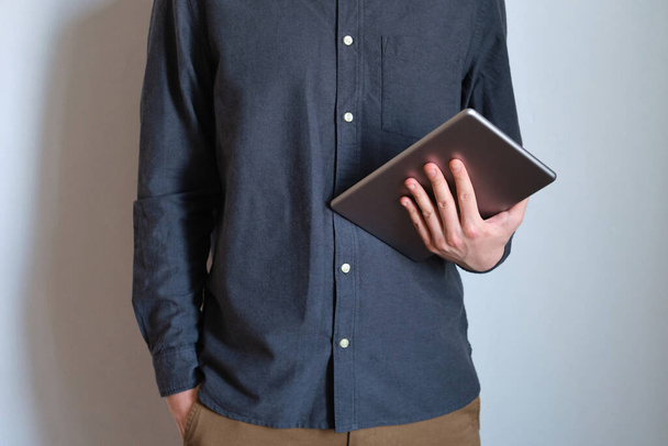 Een man met een stijlvolle tablet in zijn handen. Zakenman met een trendy draagbare gadget. Moderne technologie, draadloos internet. Mobiel toestel voor werk en vrije tijd. Vrijheid levensstijl, freelance werk - Foto, afbeelding