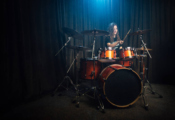 Woman playing drums and cymbals during live concert performance with band on stage in darkness lit by a spot from above with copy space - Foto, Imagen