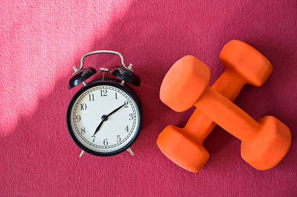 Two orange tunnels and an alarm clock on a pink yoga mat. Time to do fitness at home with equipment. Quarantine sports discipline - Foto, afbeelding