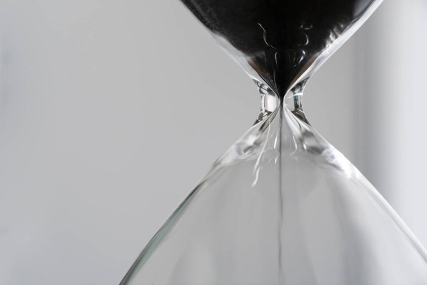 Черный песок, проходящий через лампы песочных часов, измеряя время в обратном отсчёте до делового срока, срочности и нехватки времени на светлом фоне с копировальным пространством вблизи
 - Фото, изображение